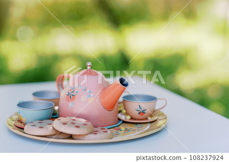 Colorful toy teapot with cups and cookies stands on a tray on a table in the garden for a tea party 108237924
