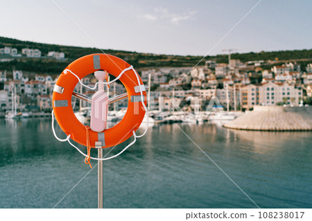 Lifebuoy on a steel post with a lock by the sea against the backdrop of colorful houses on the coast 108238017