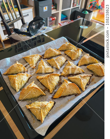 Puff pastry pies with sesame seeds lie on a tray on the table 108238623