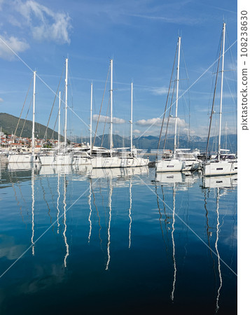 Sailing yachts with high masts reflected in the sea against the backdrop of a mountain range Sailing yachts with high masts reflected in the sea against the backdrop of a mountain range 108238630