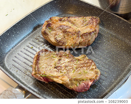 Juicy steaks with a crispy crust are fried in a grill pan on the stove Juicy steaks with a crispy crust are fried in a grill pan on the stove 108239003