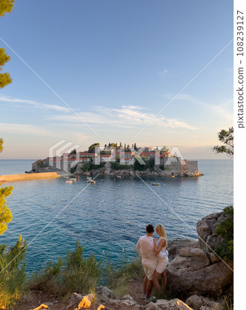 Man and woman stand hugging on the shore and look at the island of Sveti Stefan. Montenegro Man and woman stand hugging on the shore and look at the island of Sveti Stefan. Montenegro 108239127