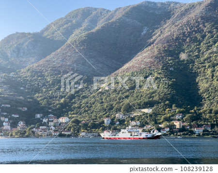 Cargo ferry sails along the sea along the coast of a small town at the foot of high mountains Cargo ferry sails along the sea along the coast of a small town at the foot of high mountains 108239128