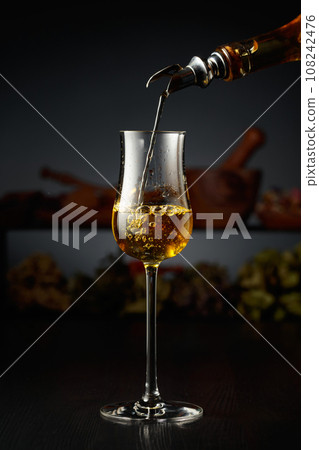 Yellow herbal liquor is poured from a vintage bottle into a glass. 108242476