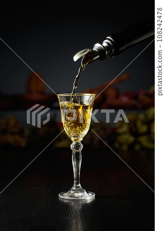Yellow herbal liquor is poured from a vintage bottle into a glass. Yellow herbal liquor is poured from a vintage bottle into a glass. 108242478