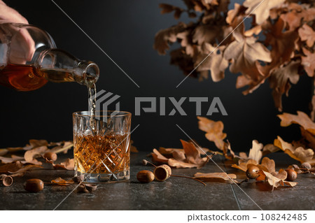Whiskey on a black table with dried-up oak leaves. Whiskey on a black table with dried-up oak leaves. 108242485