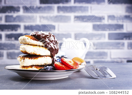 Traditional syrniki served with fresh strawberries, blueberry, mint leaves, drizzled with chocolate Traditional syrniki served with fresh strawberries, blueberry, mint leaves, drizzled with chocolate 108244552