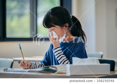 Elementary school girl holding her nose with a tissue Elementary school girl holding her nose with a tissue 108250548