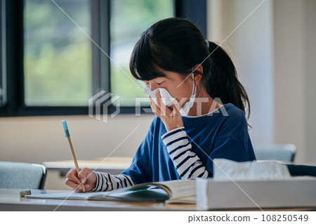 Elementary school girl holding her nose with a tissue Elementary school girl holding her nose with a tissue 108250549
