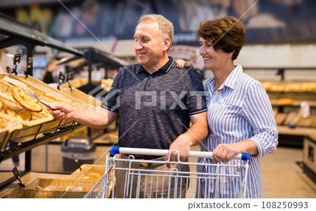 Elderly couple buys bread and baking in grocery section of supermarket Elderly couple buys bread and baking in grocery section of supermarket 108250993