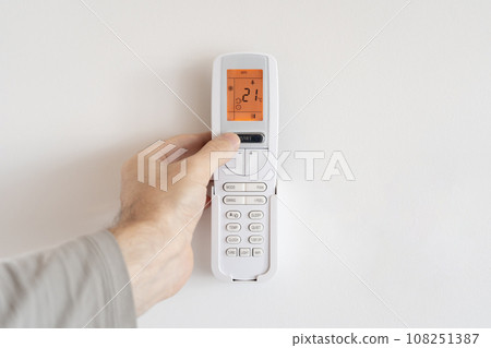 A man presses the power button on a remote control for an air conditioner. A man presses the power button on a remote control for an air conditioner. 108251387