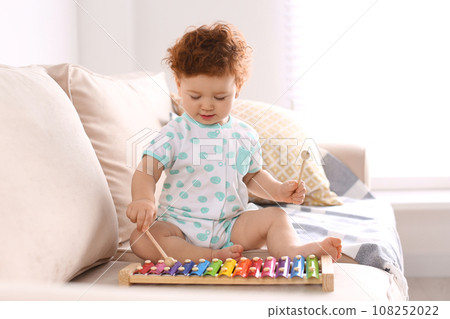 Cute little child playing with xylophone on sofa at home Cute little child playing with xylophone on sofa at home 108252022