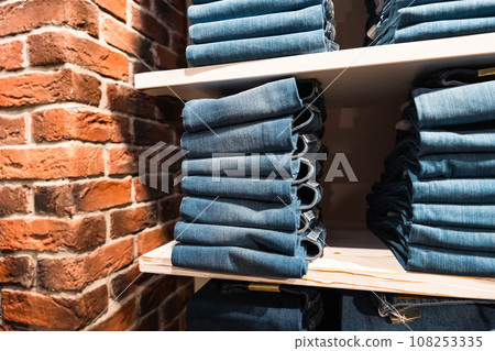 Stacks of blue denim pants are neatly laid out on a shelf in the store 108253335