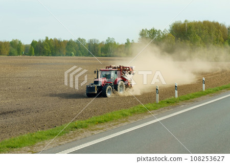 A tractor drives across a plowed field with a cloud of dust behind it. 108253627