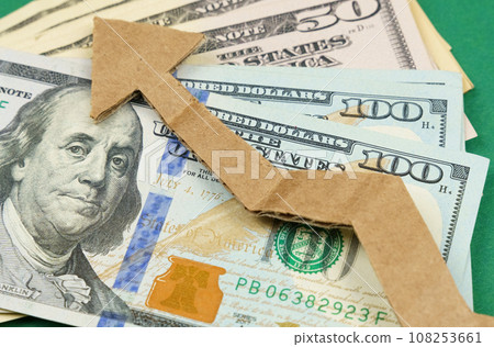 Dollars and a cardboard arrow pointing up lie on a green surface. Dollars and a cardboard arrow pointing up lie on a green surface. 108253661