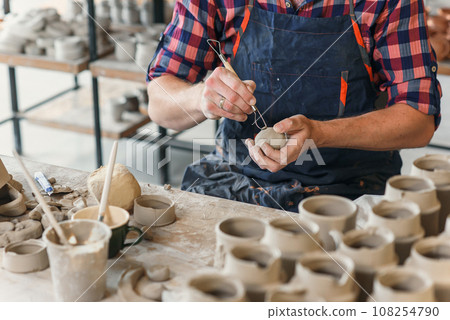 Male ceramist in the uniform works with clay at pottery workshop. 108254790