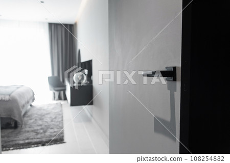 Modern black door handle and lock on black wooden hidden door. Close-up elements of the modern interior of the apartment. Modern black door handle and lock on black wooden hidden door. Close-up elements of the modern interior of the apartment. 108254882