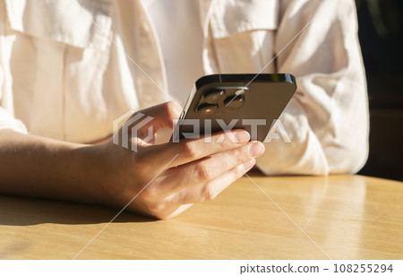 Berlin, Germany October 20 2023 Hand holding mobile phone, using smartphone, cellphone at wood cafe table 108255294