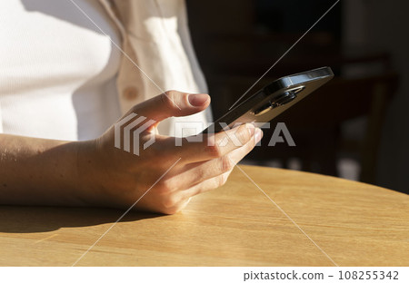 Berlin, Germany September 16 2023 Hand holding mobile phone, using smartphone at desk Berlin, Germany September 16 2023 Hand holding mobile phone, using smartphone at desk 108255342