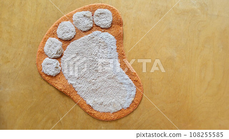 Funny fluffy rug in the shape of a foot on a beige wooden floor. 108255585