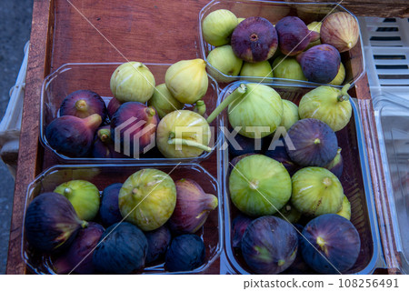 mixed green and purple figs in plastic boxes on the market. 108256491
