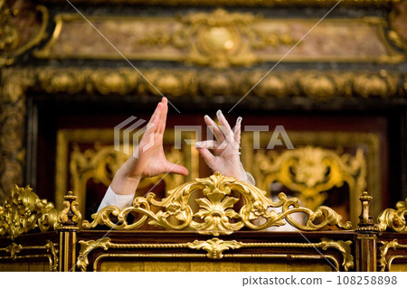 Hands gesturing in front of ornate golden decorations. Hands gesturing in front of ornate golden decorations. 108258898