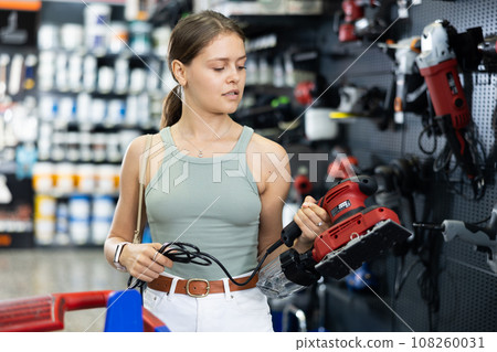 Woman choose examines grinding machine in tools department of construction store Woman choose examines grinding machine in tools department of construction store 108260031