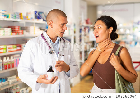 Pharmacist offering medicine for sore throat to patient at pharmacy closeup Pharmacist offering medicine for sore throat to patient at pharmacy closeup 108260064