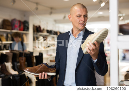 Male shopper comparing two moccasins models in shoe store 108260100