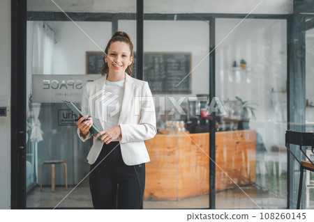 Successful businesswoman standing in creative office and looking on camera. Woman entrepreneur in a coworking space smiling. 108260145