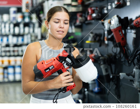 Woman chooses and buys paint spray gun in hardware store Woman chooses and buys paint spray gun in hardware store 108260161