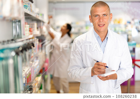 Positive pharmacist makes notes on a notebook in the sales area of pharmacy 108260238