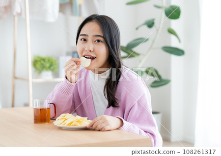 A young woman eating potato chips 108261317