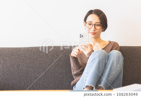 A woman wearing glasses looking at a smartphone 108263049