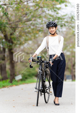 Young woman in business casual clothes walking while pushing a road bike 108263480