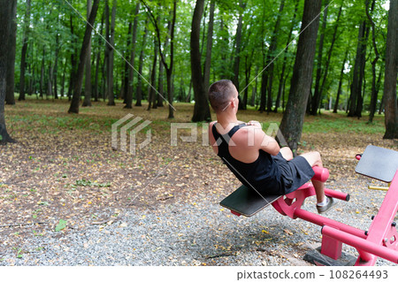 Rear view: a young man trains the abdominal muscles on a sports field in the park. Concept: fitness, healthy lifestyle, urbanism Rear view: a young man trains the abdominal muscles on a sports field in the park. Concept: fitness, healthy lifestyle, urbanism 108264493