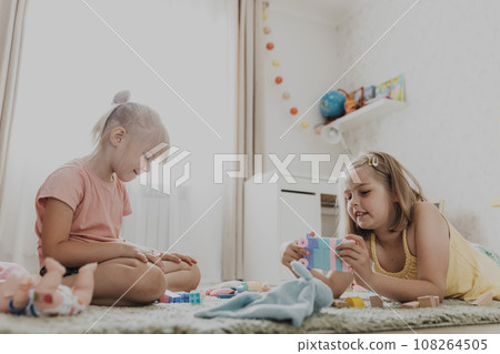 Children playing with colorful toys. Kids sitting on carpet at home bedroom or kindergarten, nursery. Educational eco-friendly game for child. Concentrated creative preschool age sweet sisters 108264505