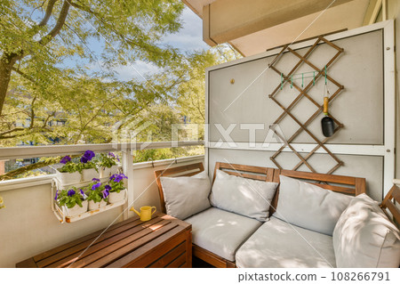 an outdoor living area with wooden furniture and plants on the balcony overlooking trees in the distance are bright blue skys an outdoor living area with wooden furniture and plants on the balcony overlooking trees in the distance are bright blue skys 108266791