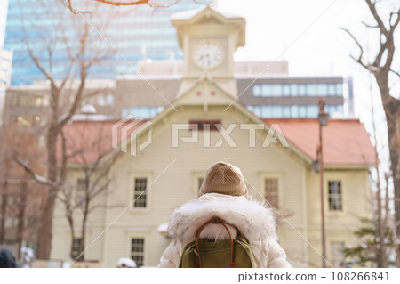 Woman tourist Visiting in Sapporo, Traveler in Sweater sightseeing Sapporo Clock tower with Snow in winter. landmark and popular for attractions in Hokkaido, Japan. Travel and Vacation concept 108266841