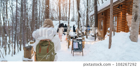 Woman tourist Visiting in Furano, Traveler in Sweater sightseeing Ningle Terrace Cottages with Snow in winter. landmark and popular for attractions in Hokkaido, Japan. Travel and Vacation concept 108267292