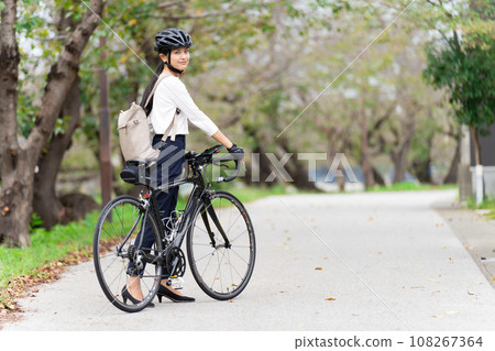 A young woman walking while pushing a road bike in business casual clothes, back view 108267364