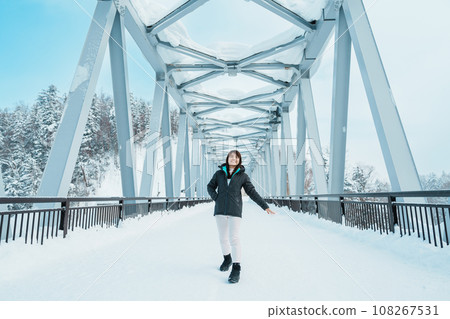 Woman tourist Visiting in Biei, Traveler in Sweater sightseeing Shirahige Waterfall bridge with Snow in winter. landmark and popular for attractions in Hokkaido, Japan. Travel and Vacation concept Woman tourist Visiting in Biei, Traveler in Sweater sightseeing Shirahige Waterfall bridge with Snow in winter. landmark and popular for attractions in Hokkaido, Japan. Travel and Vacation concept 108267531