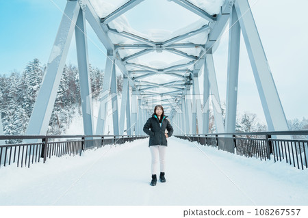 Woman tourist Visiting in Biei, Traveler in Sweater sightseeing Shirahige Waterfall bridge with Snow in winter. landmark and popular for attractions in Hokkaido, Japan. Travel and Vacation concept Woman tourist Visiting in Biei, Traveler in Sweater sightseeing Shirahige Waterfall bridge with Snow in winter. landmark and popular for attractions in Hokkaido, Japan. Travel and Vacation concept 108267557