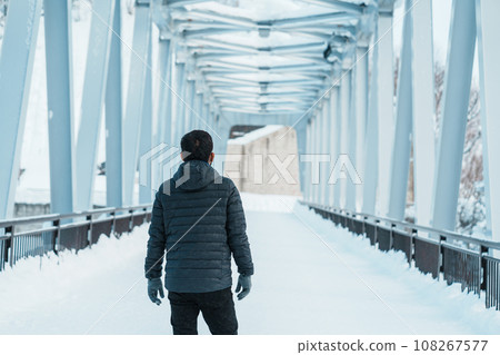 man tourist Visiting in Biei, Traveler in Sweater sightseeing Shirahige Waterfall bridge with Snow in winter. landmark and popular for attractions in Hokkaido, Japan. Travel and Vacation concept 108267577