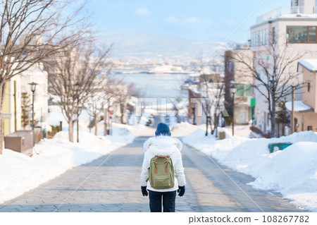 Woman tourist Visiting in Hakodate, Traveler in Sweater sightseeing Hachiman Zaka Slope with Snow in winter. landmark and popular for attractions in Hokkaido, Japan. Travel and Vacation concept 108267782