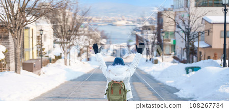 Woman tourist Visiting in Hakodate, Traveler in Sweater sightseeing Hachiman Zaka Slope with Snow in winter. landmark and popular for attractions in Hokkaido, Japan. Travel and Vacation concept 108267784