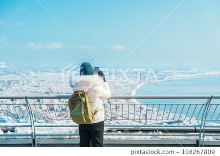 Woman tourist Visiting in Hakodate, Traveler in Sweater sightseeing view from Hakodate mountain with Snow in winter. landmark and popular for attractions in Hokkaido, Japan.Travel and Vacation concept 108267809