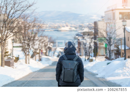 Man tourist Visiting in Hakodate, Traveler in Sweater sightseeing Hachiman Zaka Slope with Snow in winter. landmark and popular for attractions in Hokkaido, Japan. Travel and Vacation concept 108267855