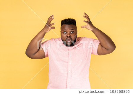 Portrait of astonished exhausted man wearing pink shirt showing explosion, looking worried and shocked, deadline, professional burnout. Indoor studio shot isolated on yellow background. 108268895
