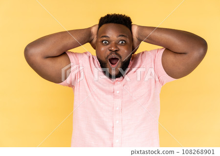 Wow amazing. Portrait of man wearing pink shirt looking at camera with wide open mouth, expressing shock and excitement about great news. Indoor studio shot isolated on yellow background. Wow amazing. Portrait of man wearing pink shirt looking at camera with wide open mouth, expressing shock and excitement about great news. Indoor studio shot isolated on yellow background. 108268901